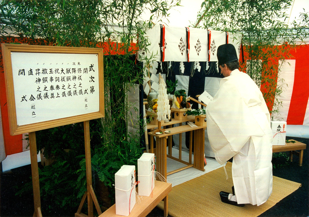 Japans ritueel bij de opening van Kikkoman in Sappemeer. Een man in een wit gewaad staat voor een tafel met onder andere allerlei fruit, wellicht een offer?