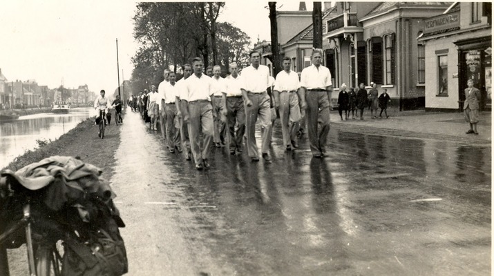 Groep jongens van Instituut Hommes wandelend midden op de straat, netjes in een rij zoals militairen dat doen, allen in schooltenue met wit hemd en lange broek.