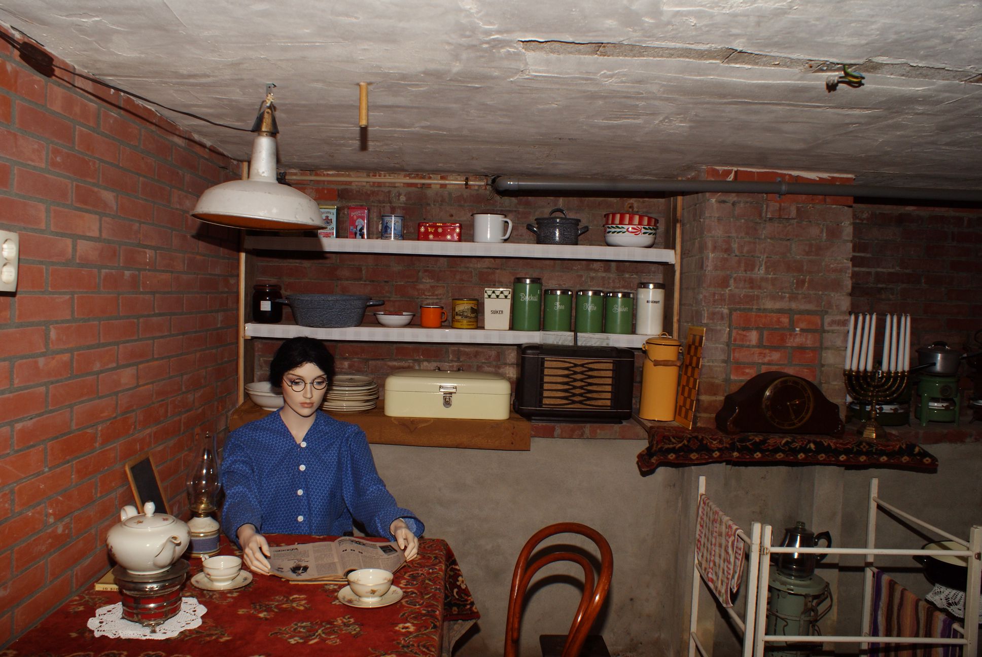 Reconstructie van de kelder met tafel met een pop eraan zittend en schappen aan de muur.