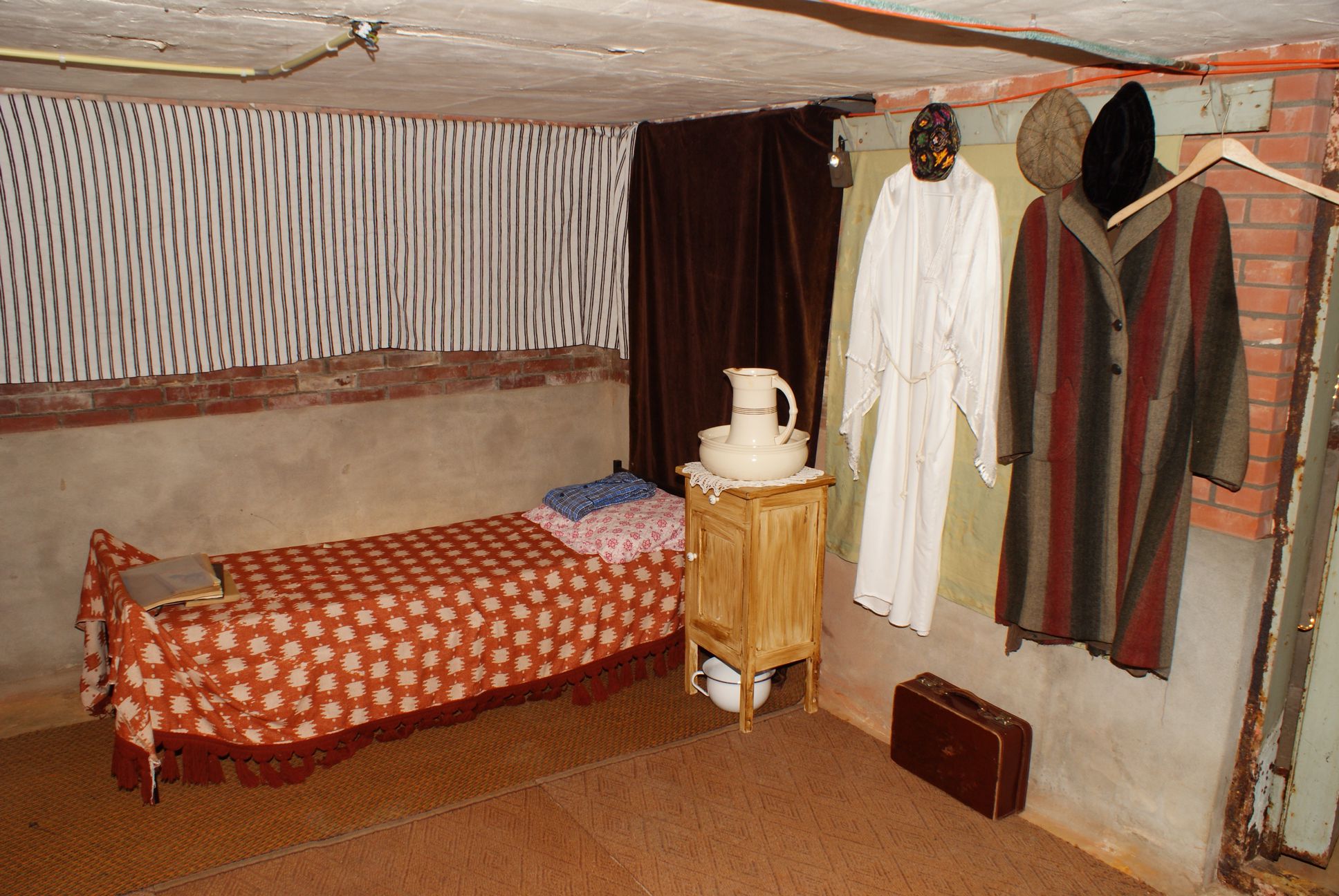Reconstructie van de kelder met een bed en een paar haakjes met kleding.