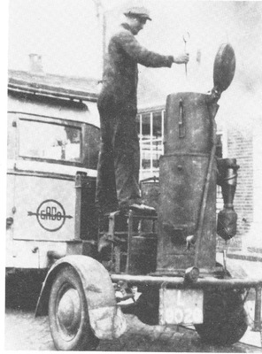 Afbeelding van een grote gasgenerator achter een bus van de Gado. De tank is open aan de bovenkant en een man is ermee bezig.