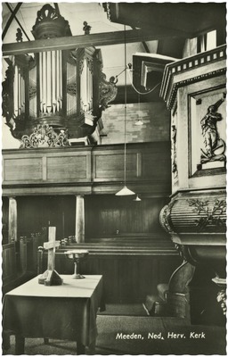 Linksboven is weer het orgel te zien, aan de rechterkant van de foto de versierde preekstoel. Onder zijn nog enkele kerkbanken te zien.