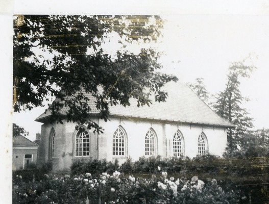 De Nederlands Hervormde Kerk in Kolham met spitsbogige ramen en bloemen op de voorgrond.
